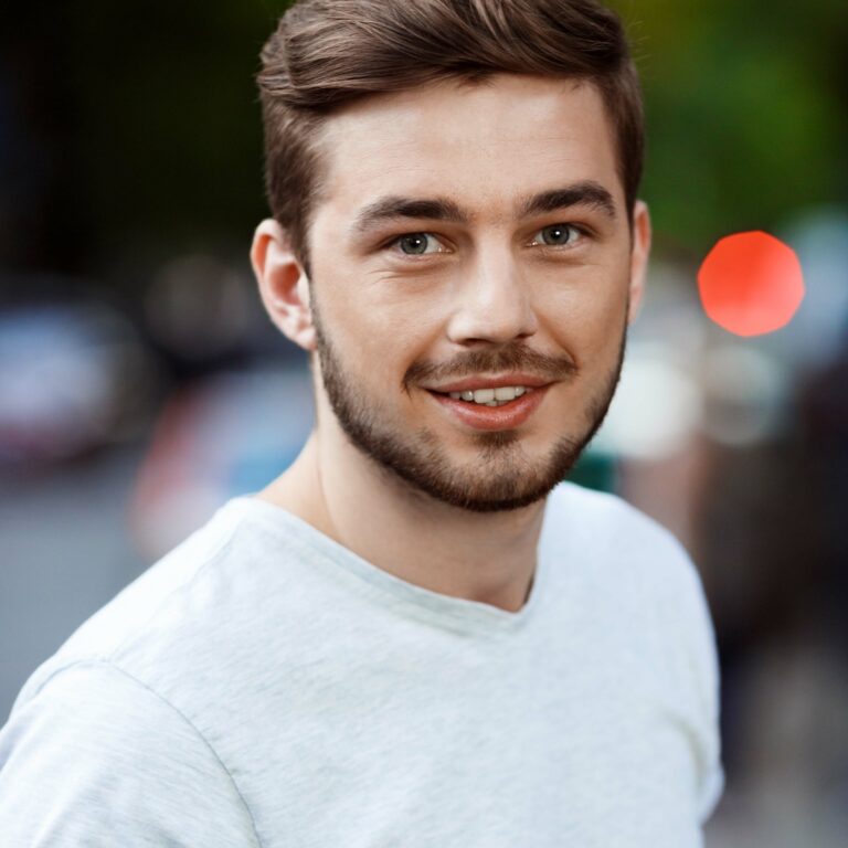 Close up portrait of handsome young man in white t-shirt looking in camera on blurry outdoor background