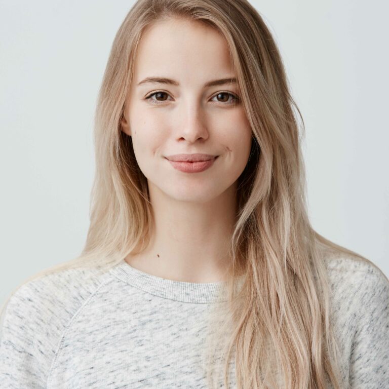 Pretty smiling joyfully female with fair hair, dressed casually, looking with satisfaction at camera, being happy. Studio shot of good-looking beautiful woman isolated against blank studio wall.